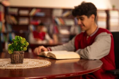 Love of culture and exploration, education and study in Saudi Arabia, visiting the school library, spending free time learning and self-education, an Arab Gulf Saudi student wearing a school uniform reading a book, developing reading skills for students, interest in browsing useful books.