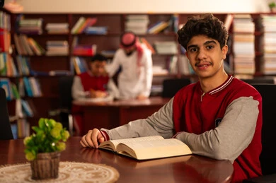 قضاء وقت الفراغ بالتعلم والتثقف الذاتي، تصوير مقرب لطالب يقوم بقراءة كتاب، معلم عربي خليجي سعودي يرتدي الثوب التقليدي والشماغ  يقوم بمناقشة الدروس مع تلميذه داخل المكتبة المدرسية، حوارات ونقاشات بين الاستاذة و الطلبة