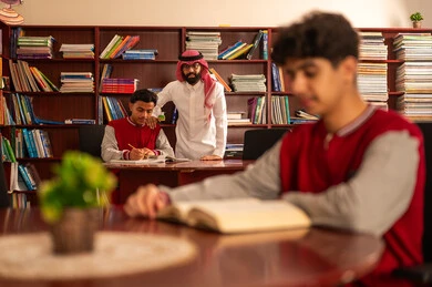 معلم عربي خليجي سعودي يرتدي الثوب التقليدي والشماغ  يقوم بمناقشة الدروس مع تلميذه داخل المكتبة المدرسية، حوارات ونقاشات بين الاستاذة و الطلبة، تصوير مقرب لطالب يقوم بقراءة كتاب، قضاء وقت الفراغ بالتعلم والتثقف الذاتي