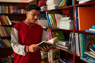 الاهتمام بالاطلاع والثقافة، زيارة مكتبة المدرسة، طالب عربي خليجي سعودي يرتدي الزي المدرسي يقف امام مكتبة خشبية يحمل بيده كتاب، تنمية مهارة القراءة للطلاب، التعليم والدراسة في السعودية ، قضاء وقت الفراغ بالتعلم والتثقف الذاتي