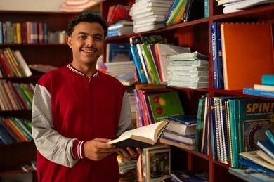 حب التعلم والاستطلاع، زيارة مكتبة المدرسة، طالب عربي خليجي سعودي يرتدي الزي المدرسي يقف امام مكتبة خشبية يحمل بيده كتاب، تنمية مهارة القراءة للطلاب، التعليم والدراسة في السعودية ، قضاء وقت الفراغ بالتعلم والتثقف الذاتي