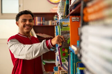 تنمية مهارة القراءة للطلاب، زيارة مكتبة المدرسة، حب الثقافة والاستطلاع، طالب عربي خليجي سعودي يرتدي الزي المدرسي يقف امام مكتبة خشبية يقوم باختيار كتاب، التعليم والدراسة في السعودية ، قضاء وقت الفراغ بالتعلم والتثقف الذاتي