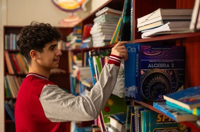 زيارة مكتبة المدرسة، حب الثقافة والاستطلاع، طالب عربي خليجي سعودي يرتدي الزي المدرسي يقف امام مكتبة خشبية يقوم باختيار كتاب، تنمية مهارة القراءة للطلاب، التعليم والدراسة في السعودية ، قضاء وقت الفراغ بالتعلم والتثقف الذاتي