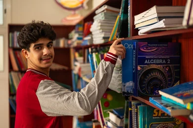 حب الثقافة والاستطلاع، زيارة مكتبة المدرسة، طالب عربي خليجي سعودي يرتدي الزي المدرسي يقف امام مكتبة خشبية يحمل بيده كتاب، تنمية مهارة القراءة للطلاب، التعليم والدراسة في السعودية ، قضاء وقت الفراغ بالتعلم والتثقف الذاتي