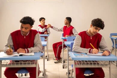 تطور طريقة التدريس في السعودية، المشاركة الفعالة للتلاميذ، النشاط داخل الفصل الدراسي، مجموعه من الطلاب العربيون الخليجيون السعوديون يرتدون الزي المدرسي يجلسون داخل الفصل، حل الواجبات المدرسية