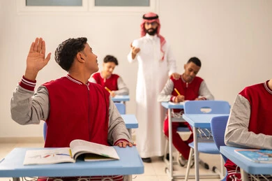 التربية والتعليم بالمناهج المقررة للطلاب في المملكة العربية السعودية، طالب عربي خليجي سعودي يرتدي الزي المدرسي يرفع يديه للإجابة، تعابير وايماءات الحماس لمعرفة الجواب الصحيح، التفاعل والمشاركة داخل الفصل الدراسي
