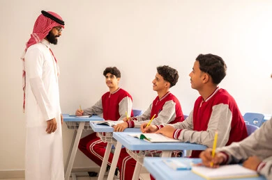 معلم عربي خليجي سعودي يرتدي ةالثوب التقليدي و الشماغ يقوم بمناقشة الدروس مع طلابه، حوارات ودية بين الاستاذ والطلاب، التربية والتعليم بالمناهج المقررة للتلاميذ، جودة التعليم في المملكة العربية السعودية، المشاركة الفعالة للطلاب مع المدرسين