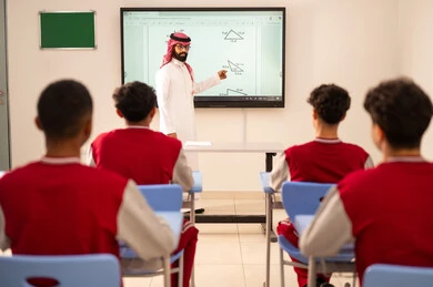 استخدام التكنولوجيا الحديثة، المناهج المطورة والتعليم الالكتروني، طلاب عربيين خليجيين سعوديين يجلسون في مقاعدهم وأمامهم مدرس سعودي يستخدم السبورة الالكترونية فى الشرح، تطور طرائق التدريس في مدارس المملكة
