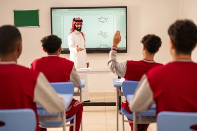 Education and teaching with the prescribed curricula for students in the Kingdom of Saudi Arabia, expressions and gestures of enthusiasm to know the correct answer, a Gulf Arab Saudi student wearing a school uniform raises his hands to answer, interaction and participation inside the classroom.