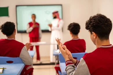 Honoring a diligent student, expressions of hands in excellence and superiority, gestures of joy and happiness, the development of teaching methods in the schools of the Kingdom, benefiting from advanced technologies in learning and studying, developed curricula and e-learning, Arab Gulf students from Saudi Arabia sitting in their seats with a Saudi teacher using an electronic board in front of them.