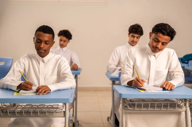 Active participation of students, gestures of contemplation and focus, goals of education and teaching, a group of Arab Gulf Saudi students wearing white thobes solving lesson questions, education in the Kingdom of Saudi Arabia.