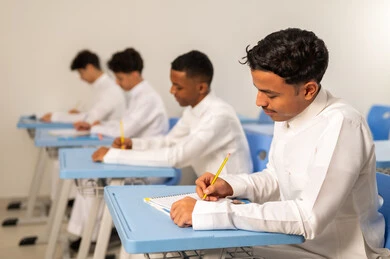 تأدية الواجبات المدرسية، التعليم في السعودية، الإستعداد للعام الدراسي الجديد، العودة إلى المدارس، مجموعة من الطلاب العربيين الخليجيين السعوديين يرتدون الثوب الابيض يجلسون في مقاعدهم ويقومون بحل الواجب