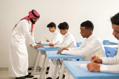 المشاركة الفعالة للطلاب مع المدرسين، مجموعة من طلاب عربيين خليجيين سعوديين يرتدون الزي المدرسي يقومون بتأديه الواجبات ، جودة التعليم في السعودية، معلم عربي خليجي سعودي يرتدي الثوب التقليدي والشماغ يقوم بمناقشة الدروس مع طلابه، التربية والتعليم بالمناهج المقررة للتلاميذ، حوارات ودية بين الاستاذ والطلاب