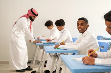مجموعة من طلاب عربيين خليجيين سعوديين يرتدون الزي المدرسي يقومون بتأديه الواجبات ، جودة التعليم في السعودية، معلم عربي خليجي سعودي يرتدي الثوب التقليدي والشماغ يقوم بمناقشة الدروس مع طلابه، المشاركة الفعالة للطلاب مع المدرسين، التربية والتعليم بالمناهج المقررة للتلاميذ، حوارات ودية بين الاستاذ والطلاب