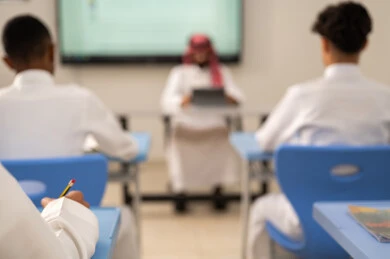 المناهج المطورة والتعليم الالكتروني، الاستفادة من التقنيات المتطورة في التعلم والدراسة، تطور طرائق التدريس في مدارس المملكة، طلاب عربيين خليجيين سعوديين يجلسون في مقاعدهم وأمامهم مدرس سعودي يستخدم التابلت فى الشرح