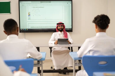 الاستفادة من التقنيات المتطورة في التعلم والدراسة، تطور طرائق التدريس في مدارس المملكة، المناهج المطورة والتعليم الالكتروني، طلاب عربيين خليجيين سعوديين يجلسون في مقاعدهم وأمامهم مدرس سعودي يستخدم التابلت فى الشرح