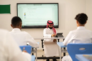 تطور طرائق التدريس في مدارس المملكة، الاستفادة من التقنيات المتطورة في التعلم والدراسة، المناهج المطورة والتعليم الالكتروني، طلاب عربيين خليجيين سعوديين يجلسون في مقاعدهم وأمامهم مدرس سعودي يستخدم التابلت فى الشرح