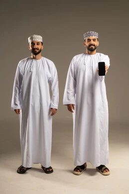 عرض شاشة جوال سوداء، دمج التقنيات التكنولوجية في الحياة اليومية، بورتريه لرجلين عربيين خليجيين عمانيين يرتديان الدشداشة و الكمة ينظران الى الكاميرا بسعادة, خلفية رمادية