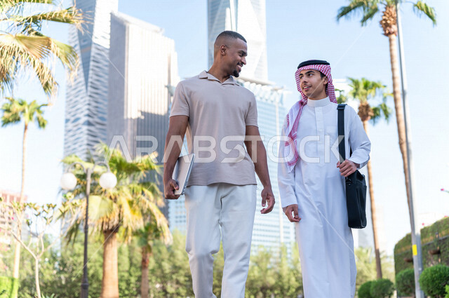 شابان عربيان خليجيان سعوديان يمارسان رياضة المشي في في إحدي منتزهات الرياض ، الاستجمام و التنزه في الهواء الطلق ، قضاء وقت ممتع في مدينة الملك عبد الله المالية ( كافد ) في مدينة الرياض ، المملكة العربية السعودية