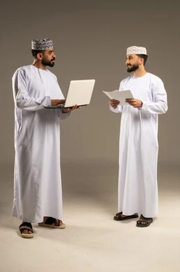 تبادل الخبرات والمهارات بين الزملاء، بورتريه لرجلين عربيين خليجيين عمانيين يرتديان الدشداشة و الكمة يستخدم أحدهما اللابتوب و يحمل الاخر ورق ابيض, خلفية رمادية