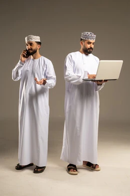 انجاز المهام و إدارة شؤون العمل عبر التكنولوجية, بورتريه لرجلين عربيين خليجيين عمانيين يرتديان الدشداشة و الكمة يستخدم أحدهما اللابتوب و يتحدث الاخر عبر الهاتف المحمول, خلفية رمادية