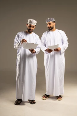 الوحده و العمل الجماعي، تقسيم و توزيع المهام، بورتريه لرجلين عربيين خليجيين عمانيين يرتديان الدشداشة و الكمة يحملان اوراق بيضاء, خلفية رمادية
