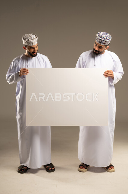 استخدام السبورة لسهولة الشرح، توضيح الاجراءات المتبعة, بورتريه لرجلين عربيين خليجيين عمانيين يرتديان الدشداشة و الكمة و يحملان لوحه بيضاء فارغه, خلفية رمادية