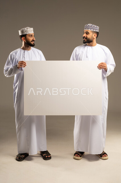 Using an educational visual aid, ensuring clear understanding using the blackboard, a portrait of two Omani Gulf Arab men wearing dishdashas and kumas looking at each other, gray background