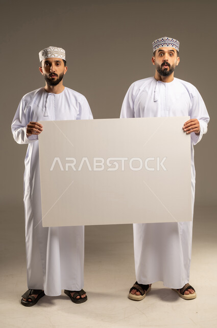 تعبير الاندهاش والانبهار, استعمال السبورة لتوضيح الاجراءات المتبعة, بورتريه لرجلين عربيين خليجيين عمانيين يرتديان الدشداشة و الكمة و ينظران الى الكاميرا بدهشة, خلفية رمادية