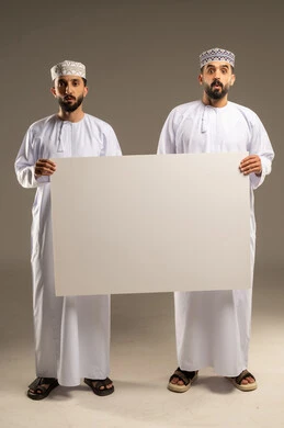 Expressions of surprise and amazement; use of a whiteboard to illustrate procedures; portrait of two Omani Gulf Arab men wearing dishdashas and kumas, looking at the camera in astonishment; gray background.