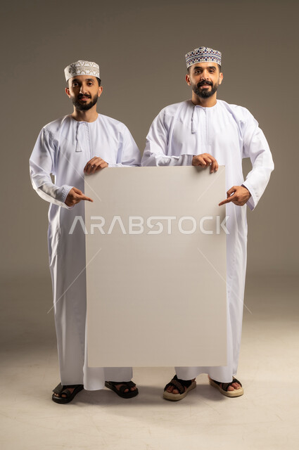 استعمال السبورة لتوضيح الاجراءات المتبعة, الاشاره بالسبابه الى لوحه بيضاء فارغه, بورتريه لرجلين عربيين خليجيين عمانيين يرتديان الدشداشة و الكمة و ينظران الى الكاميرا بسعادة, خلفية رمادية