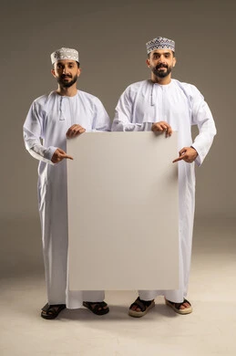 Using a whiteboard to illustrate procedures, pointing with an index finger to a blank whiteboard, a portrait of two Omani Gulf Arab men wearing dishdashas and kumas, looking happily at the camera, gray background