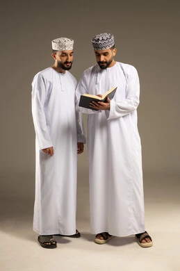 الاهتمام بتصفح الكتب, بورتريه لرجلين عربيين خليجيين عمانيين يرتديان الدشداشة و الكمة يمسك أحدهما كتاب و يقومان بمطالعته, خلفية رمادية