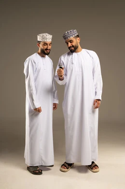 ممارسة موهبة الغناء، تعابير التركيز و التفاعل مع الموسيقى, بورتريه لرجلين عربيين خليجيين عمانيين يرتديان الدشداشة و الكمة يمسك أحدهما المايكروفون, خلفية رمادية