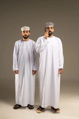 عملية البحث و التدقيق، بورتريه لرجلين عربيين خليجيين عمانيين يرتديان الدشداشة و الكمة يستخدم أحدهما العدسة المكبرة و ينظر الاخر نظرة اندهاش, خلفية رمادية