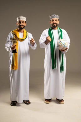 تشجيع المنتخب الوطني,  ارتداء الأوشحة التشجيعية, بورتريه لرجلين عربيين خليجيين عمانيين يرتديان الدشداشة و الكمة يمسك أحدهما بالكرة و الاخر يحمل كأس ذهبي و يرفعان قبضتيهما علامة النصر, خلفية رمادية