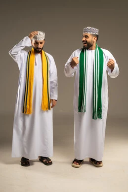 تعابير التفاعل مع نتائج المباراة, الفرح بالنصر و الفوز، إيماءات الحزن لخسارة الفريق، ارتداء الأوشحة التشجيعية, بورتريه لرجلين عربيين خليجيين عمانيين يرتديان الدشداشة و الكمة  يقوم أحدهما بإغاظة الآخر, خلفية رمادية