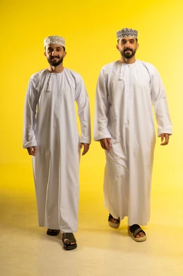 Taking a leisurely stroll, confidently walking the streets of Oman, enjoying time with friends, a portrait of two Omani Gulf Arab men wearing dishdashas and kumas, looking happily at the camera, yellow background Taking a leisurely stroll, confidently walking the streets of Oman, enjoying time with friends, a portrait of two Omani Gulf Arab men wearing dishdashas and kumas, looking happily at the camera, yellow background