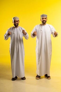 فرحة الانتصار و الفوز, متابعة مباراة كرة القدم، بورتريه لرجلين عربيين خليجيين عمانيين يرتديان الدشداشة و الكمة يرفعان قبضتيهما علامة النصر,  ايماءات السعادة و السرور, خلفية صفراء