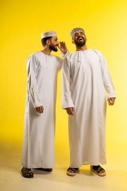 كتمان و حفظ الاسرار،  بورتريه لرجلين عربيين خليجيين عمانيين يرتديان الدشداشة و الكمة و يقوم أحدهما بالهمس في اذن صديقه, التحدث بصوت منخفض، تعبير الضحك و السعادة, خلفية صفراء