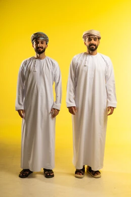 عرض ازياء رجاليه عمانيه شعبيه, الأناقة و الاهتمام بالمظهر الخارجي، بورتريه لرجلين عربيين خليجيين عمانيين يرتديان الدشداشة و العمامة ينظران الى الكاميرا بسعادة, خلفية صفراء