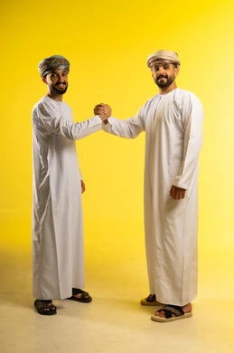دعم العلاقات الودية بين الأصدقاء, إلقاء التحية و السلام, بورتريه لرجلين عربيين خليجيين عمانيين يرتديان الدشداشة و العمامة و يسلمان على بعضهما، النظر الى الكاميرا بايماءات السعادة و السرور, خلفية صفراء
