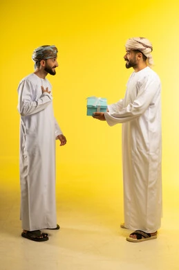 مفاجآت و أعياد سعيدة, زيادة روابط المحبة بتقديم الهدايا, التعبير عن الحب و التقدير، بورتريه لرجلين عربيين خليجيين عمانيين يرتديان الدشداشة و العمامة يهدي أحدهما الاخر هدية, ايماءات الشكر و الامتنان, خلفية صفراء