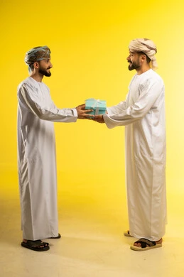 زيادة روابط المحبة بتقديم الهدايا بالمناسبات, مفاجآت و أعياد سعيدة, التعبير عن الحب والتقدير والاحترام، بورتريه لرجلين عربيين خليجيين عمانيين يرتديان الدشداشة و العمامة يهدي أحدهما الاخر هدية, خلفية صفراء