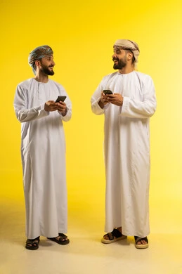 قضاء اوقات ممتعة بتبادل الأحاديث، الإجابة و الرد على الاتصالات، استخدام جهاز تقني حديث و متطور، بورتريه لرجلين عربيين خليجيين عمانيين يرتديان الدشداشة و العمامة يستخدمان الموبايل, الإستمتاع مع الأصدقاء, ايماءات السعادة و السرور, خلفية صفراء
