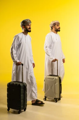 الاجازة و الرحلات الممتعة، الاستعداد و تجهيز الأمتعة استعداد لجولة سياحية، مفهوم السياحة و الترفيه، بورتريه لرجلين عربيين خليجيين عمانيين يرتديان الدشداشة و العمامة يمسكان حقائب السفر, خلفية صفراء