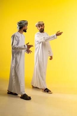 التنزه في شوارع سلطنة عمان, ممارسة رياضة المشي, نزهة لإحدى الأماكن الترفيهية، الإستمتاع مع الأصدقاء, الحوار أثناء التمشية, بورتريه لرجلين عربيين خليجيين عمانيين يرتديان الدشداشة و العمامة يقومان بالتحدث معا, خلفية صفراء
