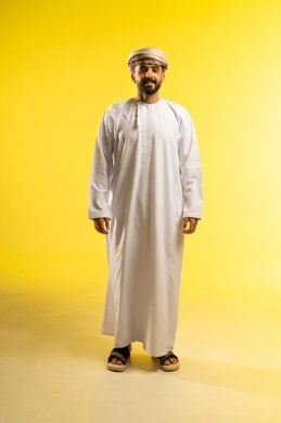 النظر الى الكاميرا بايماءات السعادة, مفهوم الرجولة و القوة، الأناقة و الاهتمام بالمظهر الخارجي، بورتريه لرجل عربي خليجي عماني يرتدي الدشداشة و العمامة و تظهر عليه تعابير الثقة بالنفس، خلفية صفراء