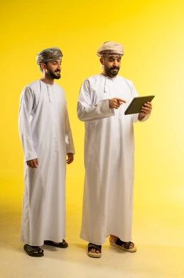 تصفح مواقع التواصل الاجتماعي، متابعة الأفلام والمسلسلات الممتعة، استخدام التقنيات الحديثة, المحادثة مع الأصدقاء, بورتريه لرجلين عربيين خليجيين عمانيين يرتديان الدشداشة و العمامة يمسك أحدهما جهاز التابلت, خلفية صفراء