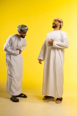 Laughing and chatting with friends, sharing enjoyable moments, friendship and building relationships, a portrait of two Arab Gulf Omani men wearing the dishdasha and turban laughing together, gestures of happiness and joy, yellow background.